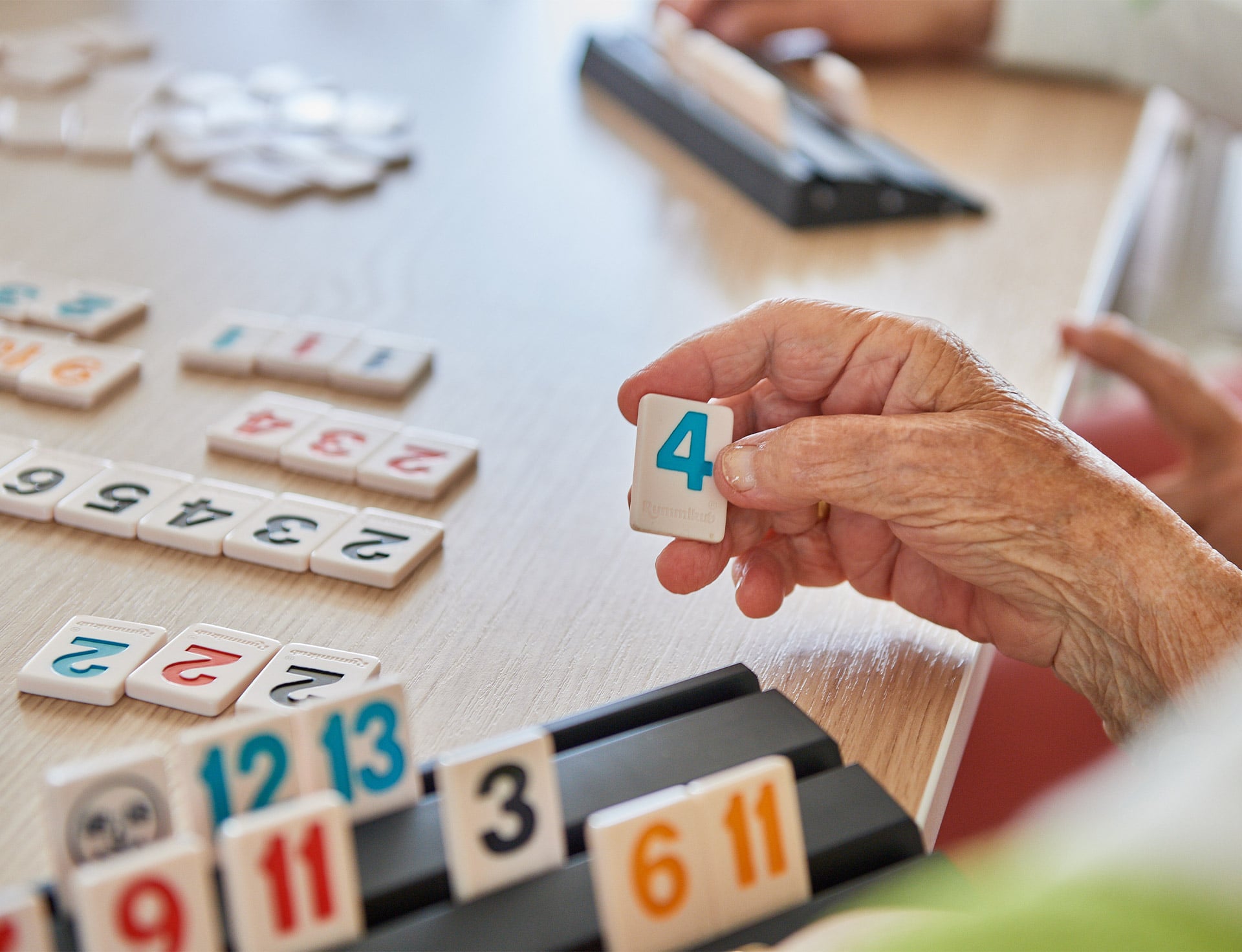 Evdiak Bild einer Seniorenhand mit Rummikub Steinen vor sich