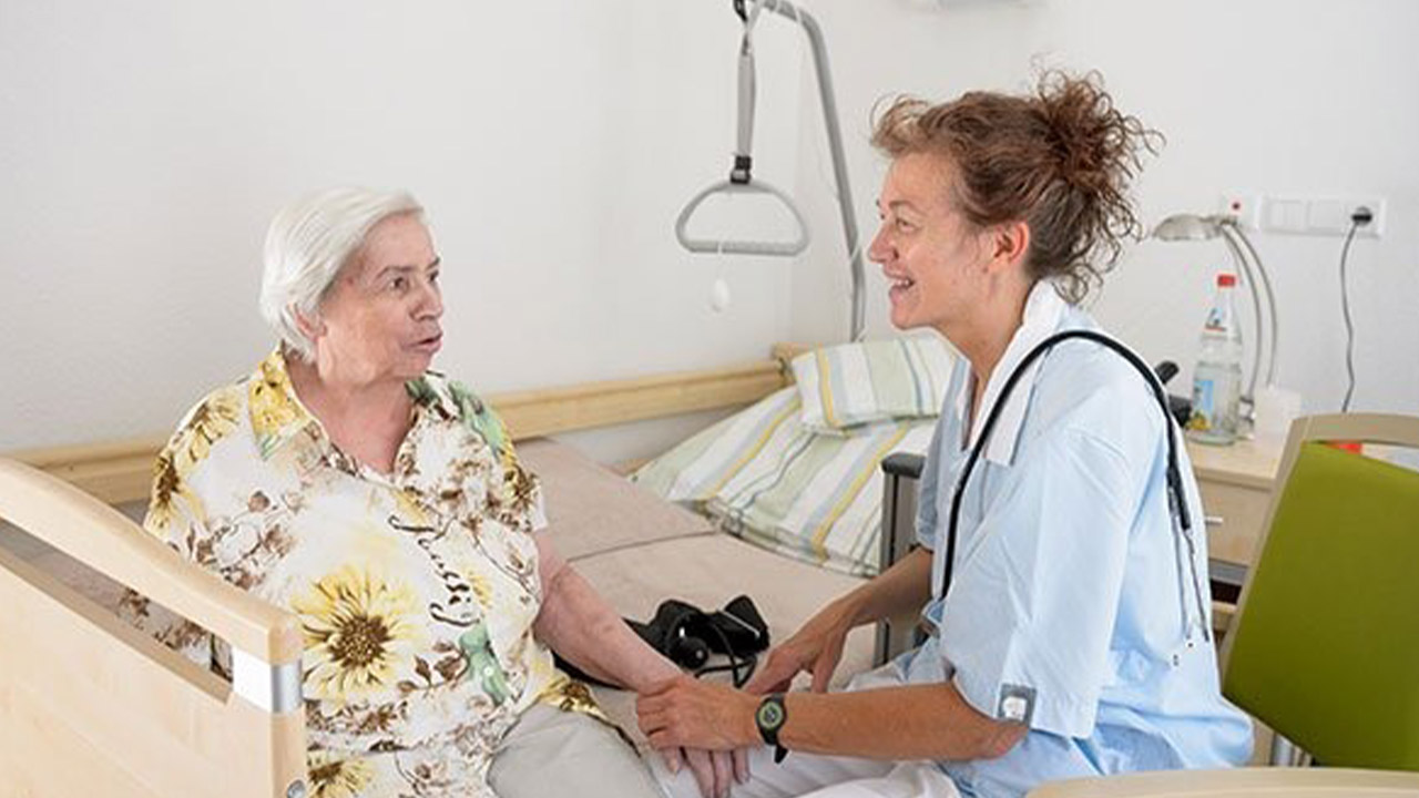 Evdiak Bild von einer Senioren auf dem Bett sitzend und einer Pflegerin