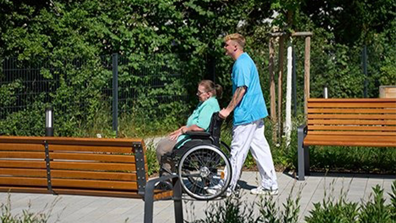 Evdiak Bild von einem Pfleger, der eine Seniorin im Rollstuhl schiebt