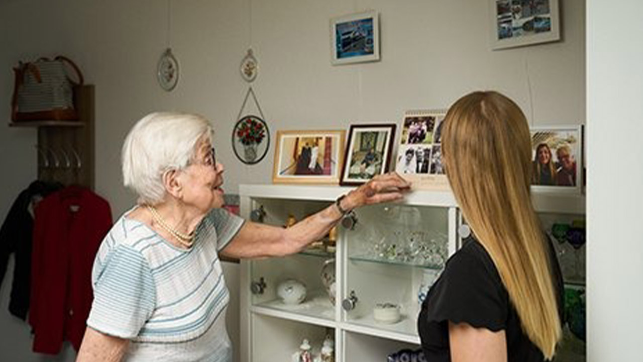 Evdiak Bild von einer Seniorin und einer jüngeren Frau, die Seniorin zeigt ihre Familienbilder