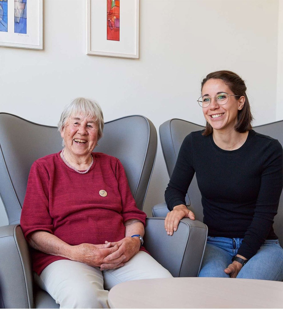 Evdiak Foto Eine Seniorin und eine junge Pfelegerin sitzen gelassen und fröhlich auf zwei Sesseln