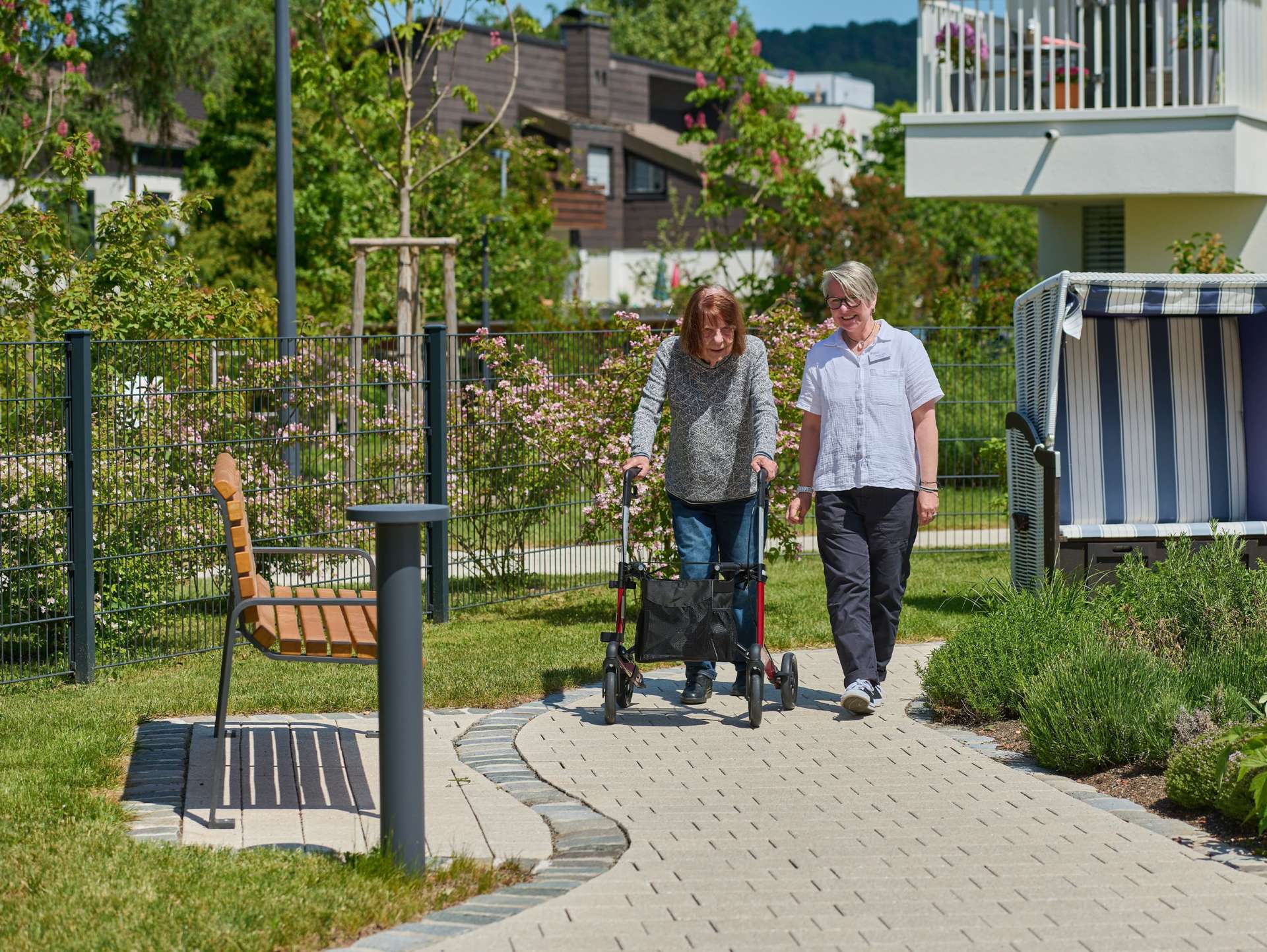 Evdiak Bild einer Seniorin mit Rollator und einer Mitarbeiterin, beide laufen gemeinsam durch den Garten
