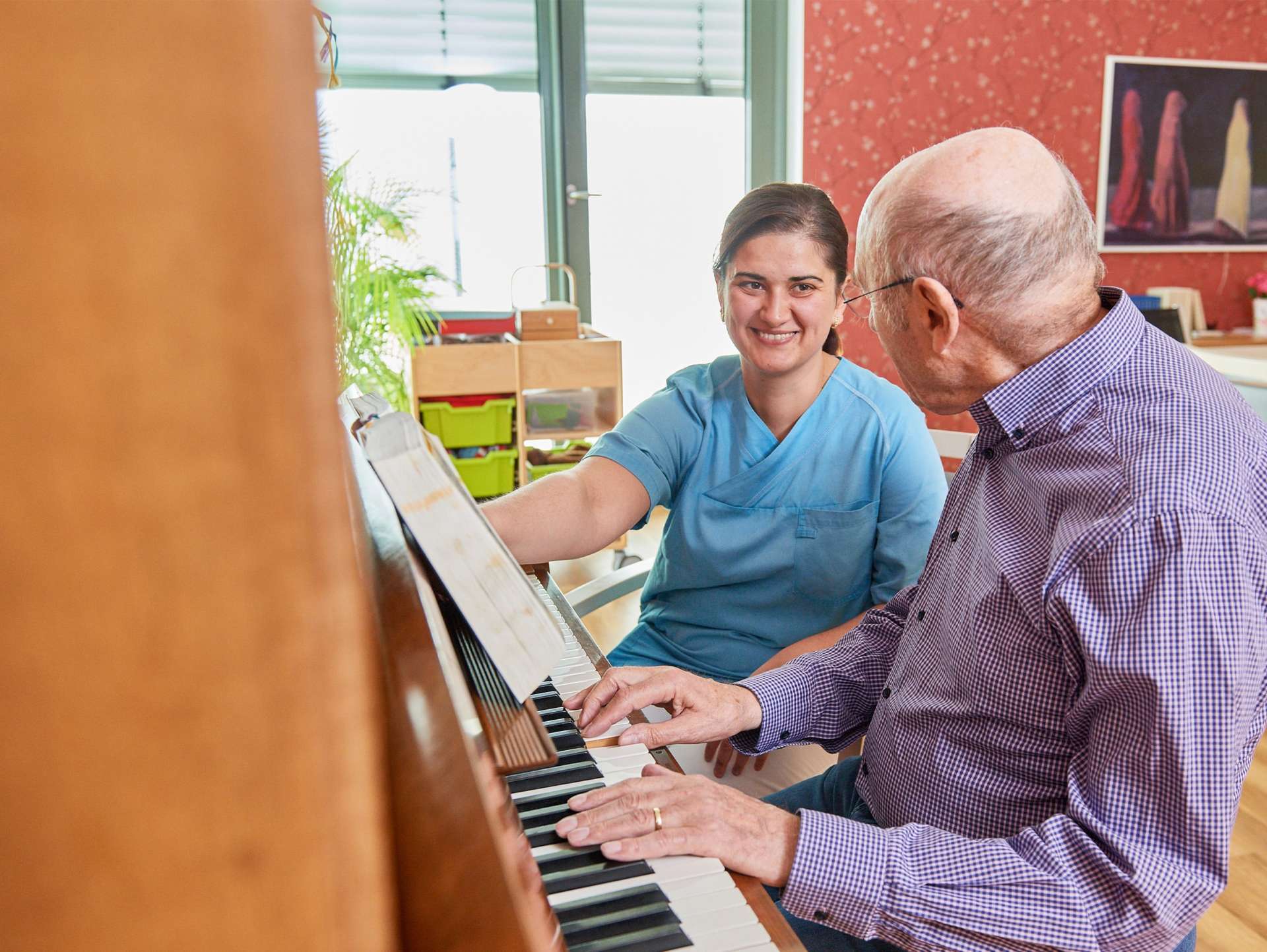 Evdiak Bild von einer Pflegerin und einem Senior, die gemeinsam an einem Klavier sitzen