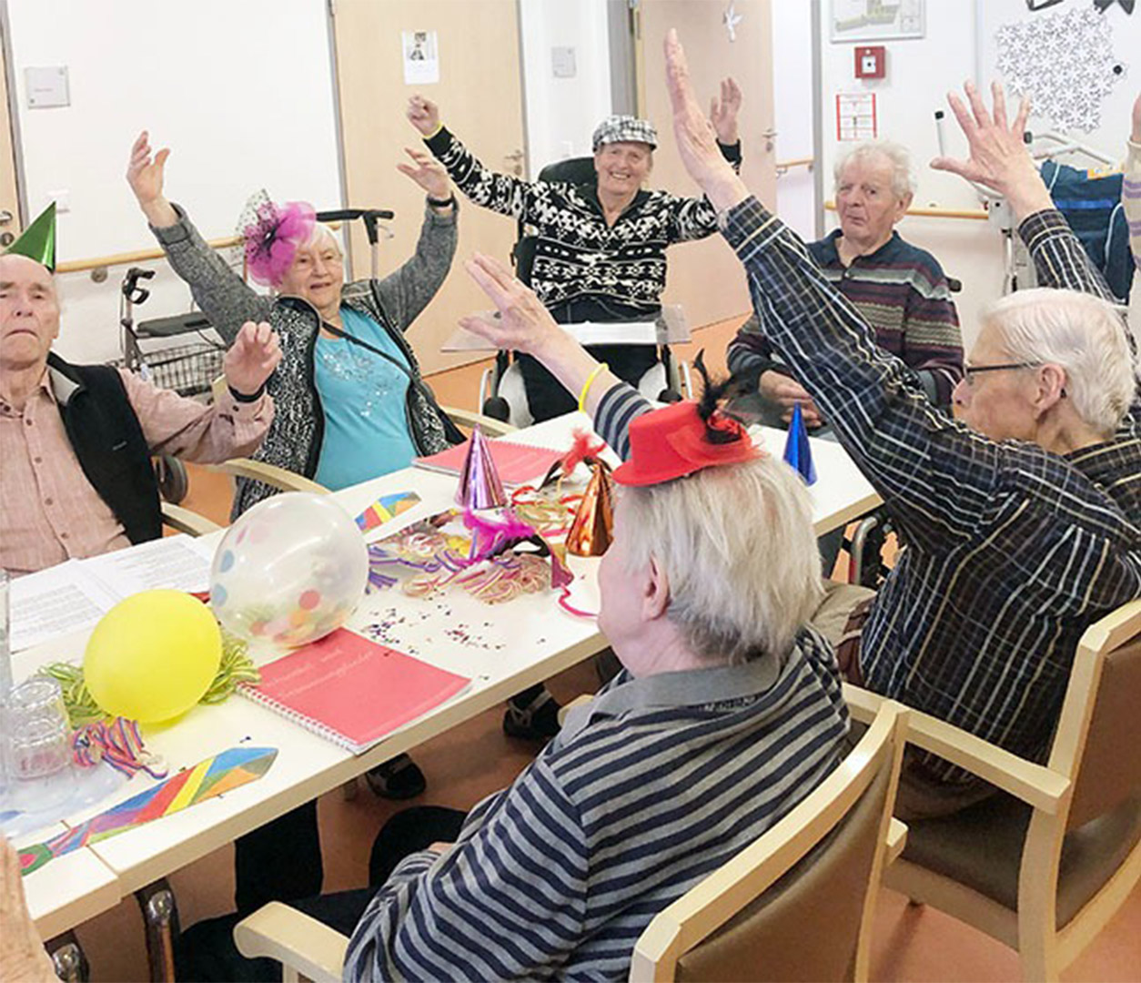 Evdiak Bild von Senioren an einem Tisch, die die Hände in die Luft strecken und lächeln