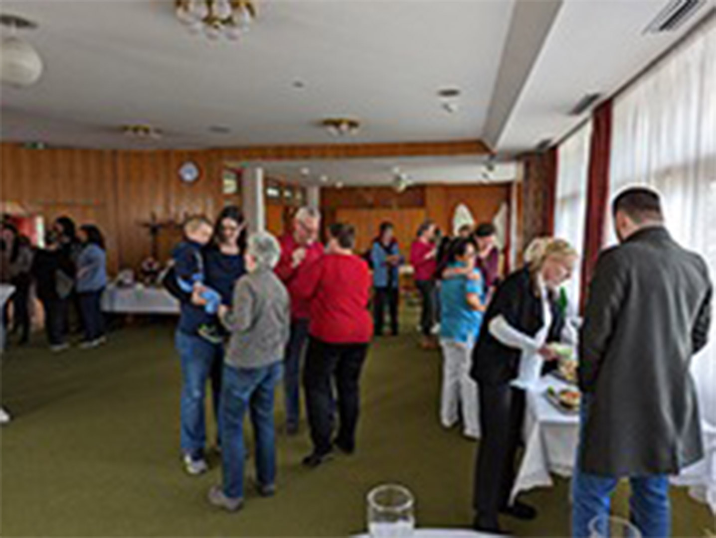 Evdiak Bild von einem Raum mit verschiednen Personen, die sich unterhalten. Rechts ist ein Buffet