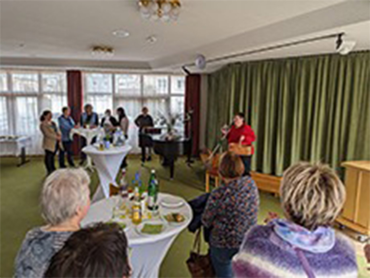 Evdiak Bild von einem Raum mit mehreren Personen verteilt an Stehtischen, eine Frau spricht in ein Mikrofon