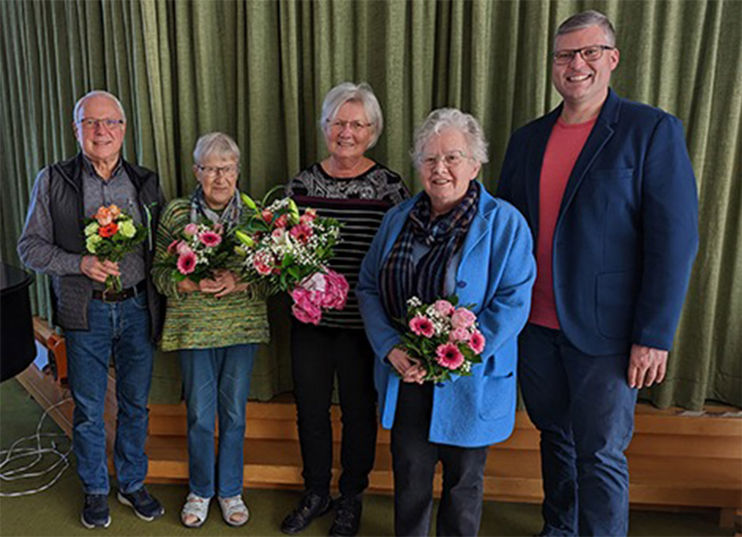 Evdiak Bild von fünf Personen vor einem grünen Hintergund. Alle lächeln und vier Personen halten einen Blumenstrauß in den Händen