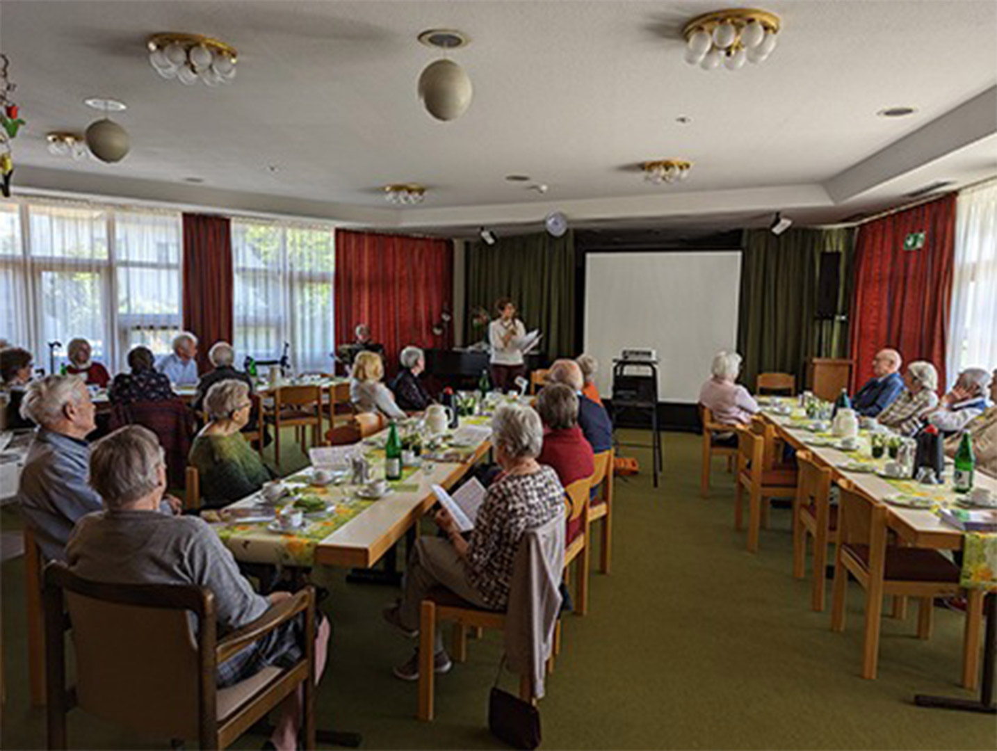 Evdiak Bild von Senioren, die an Tischen sitzen und auf eine Bühne schauen