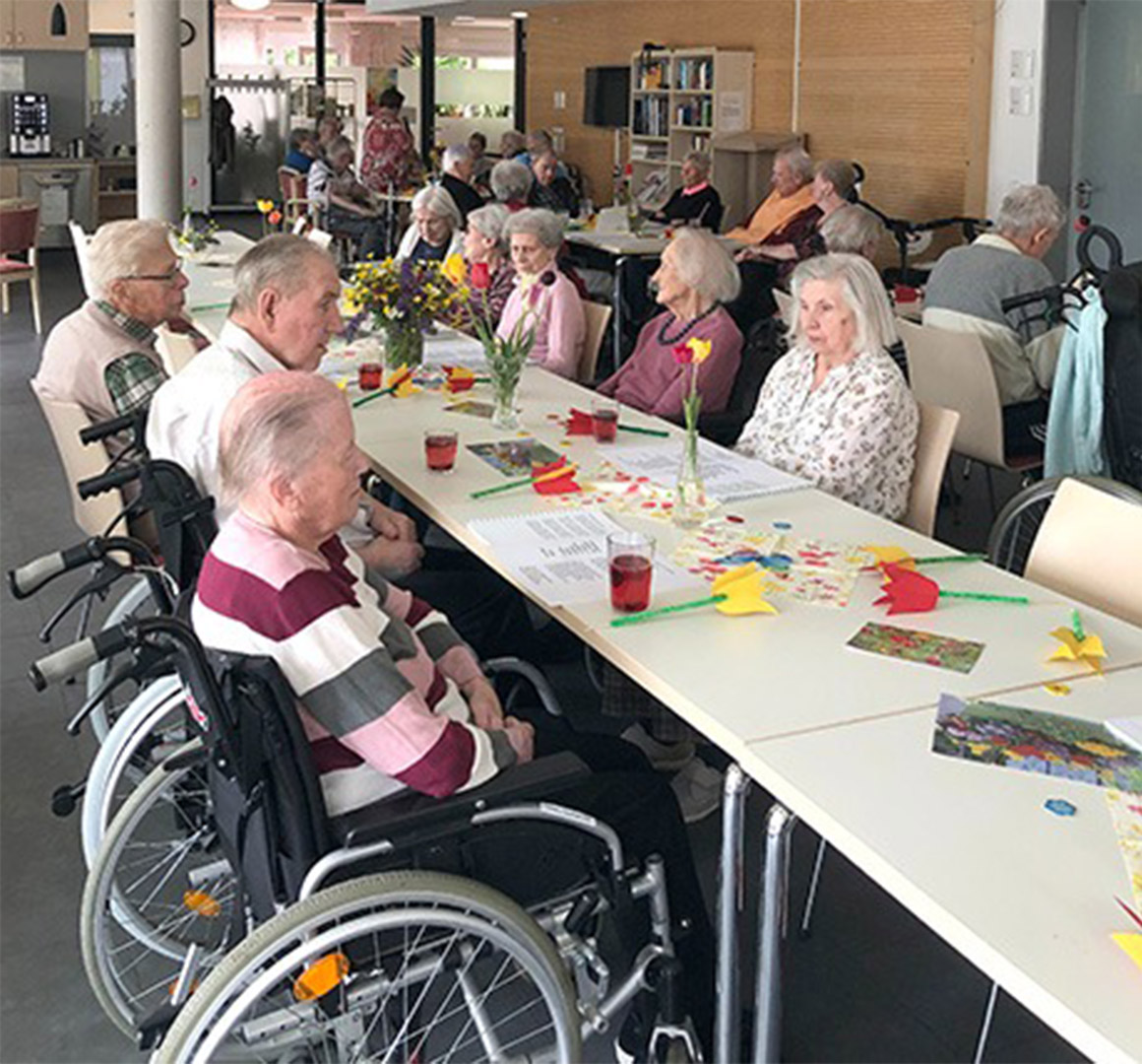 Evdiak Bild eines Tisches, an dem Senioren sitzen und bunte Papierblumen vor sich haben