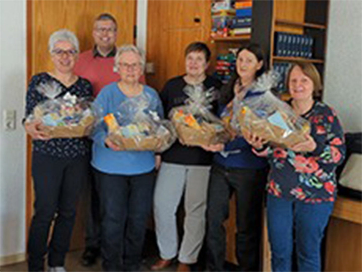 Evdiak Bild von sechs Personen, sie stehen nebeneinander und halten Abschiedsgeschenke in den Händen