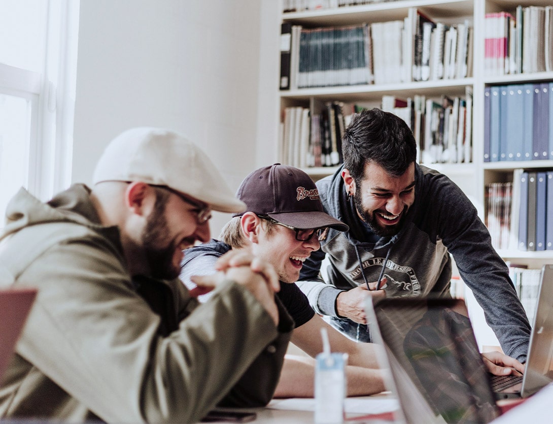 Evdiak Foto von 3 jungen Männern, die in einem Büro vor einem Laptop sitzen und lachen