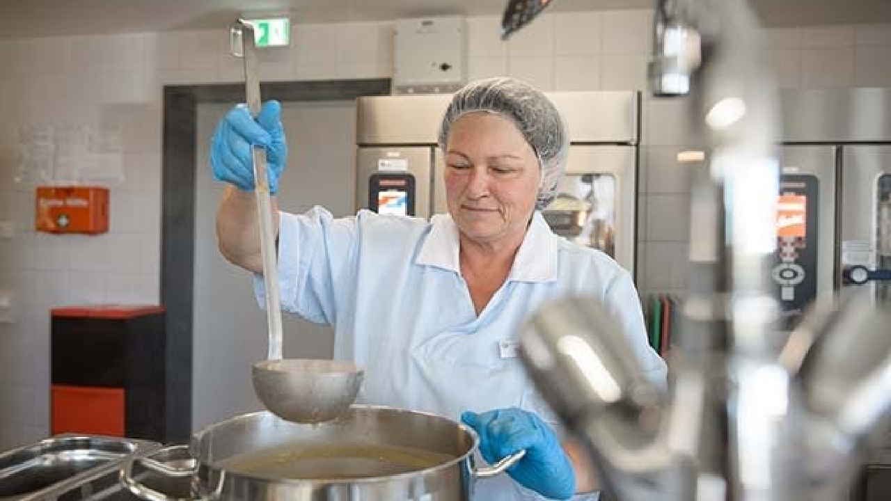 Evdiak Köchin mit Schöpflöffel und einem großen Suppentopf in der Küche der Einrichtung